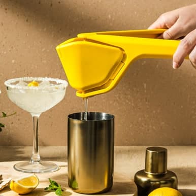 Yellow Dreamfarm Fluicer squeezing citrus over a metal cup