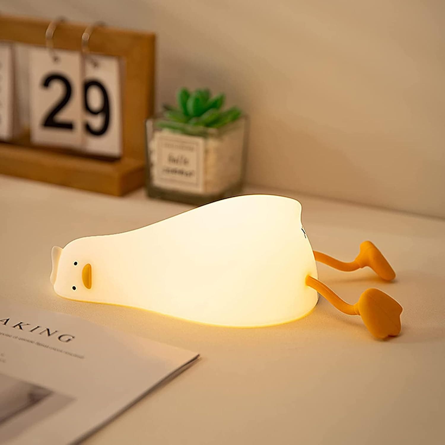 Glowing HAPPYBAG lying-flat duck night light on a bedside table