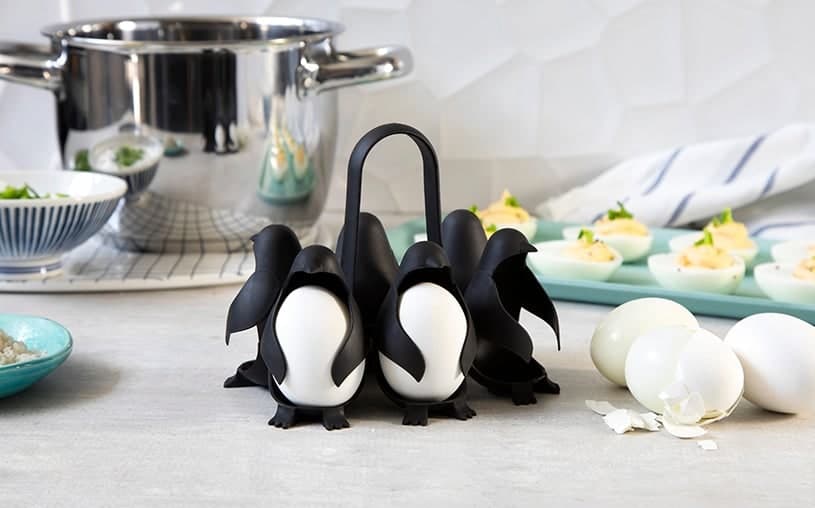 Six black penguin-shaped egg holders beside a cooking pot